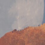 Teide Yanardağı’nın Ardında Batan Ay Group of hikers standing on a rocky ridge at the edge of a cliff with a pale sky behind them